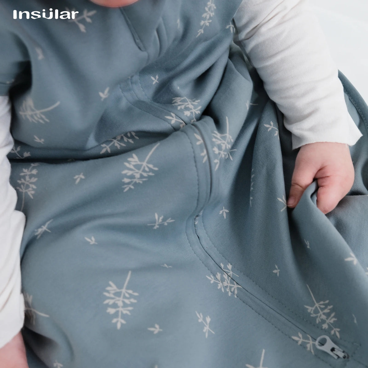 A close-up of a baby wearing a soft, light blue cotton sleep sack with a subtle white snowflake pattern.