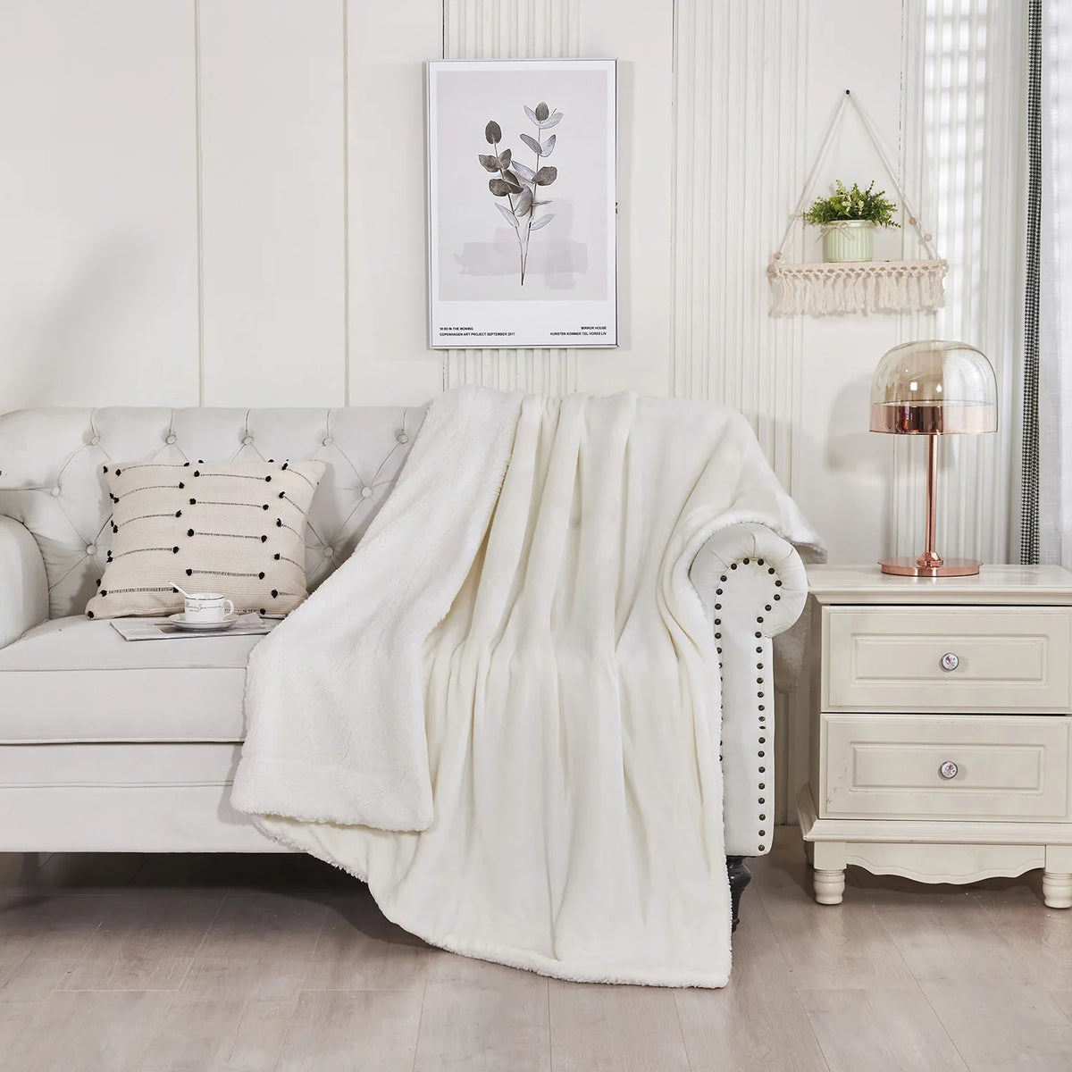 A fluffy white sherpa fleece blanket draped over a light gray sofa in a bright, modern room.