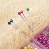 A collection of colorful pearl head sewing pins in various shades are displayed on a burlap fabric.