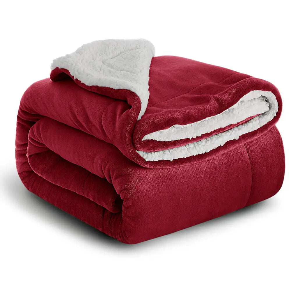A deep red sherpa fleece blanket with a white fluffy trim, rolled up and displayed on a white background.
