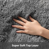 A hand is touching a gray, fluffy top layer of a plush floor mat.