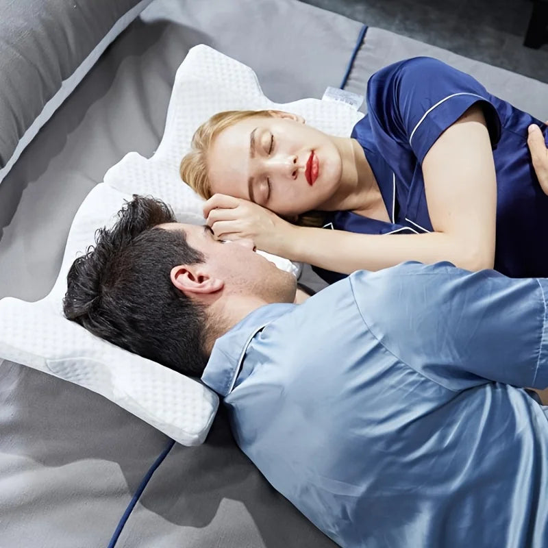 A woman gently cuddles a man while they rest on a gray memory foam pillow.