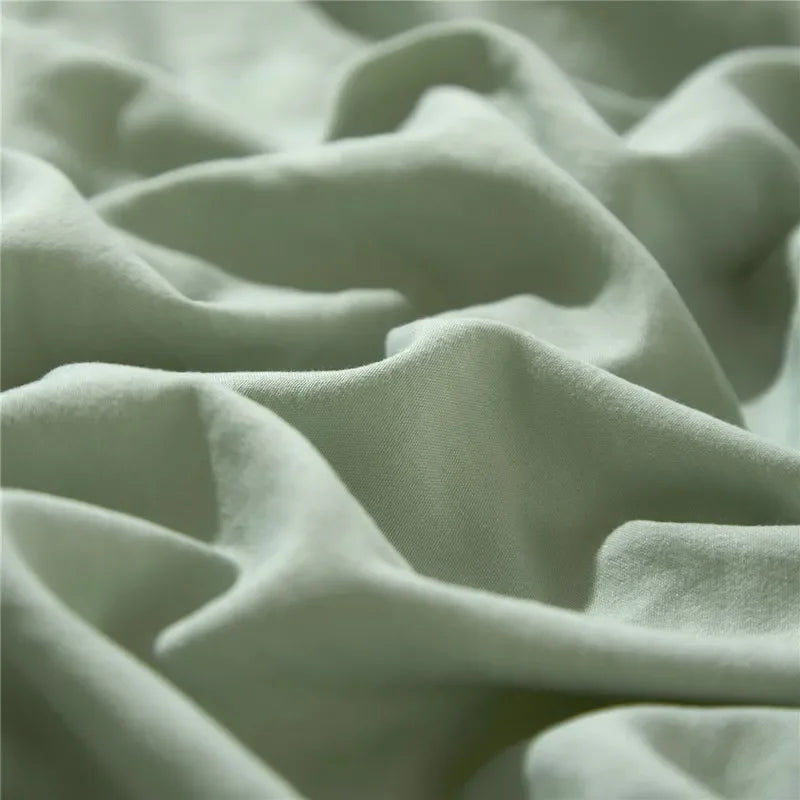 Close-up of a soft sage green duvet cover set with visible folds and pom-pom texture.