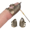 A hand holds an antique sewing thimble and needle protector set featuring textured brass or bronze metal pieces.