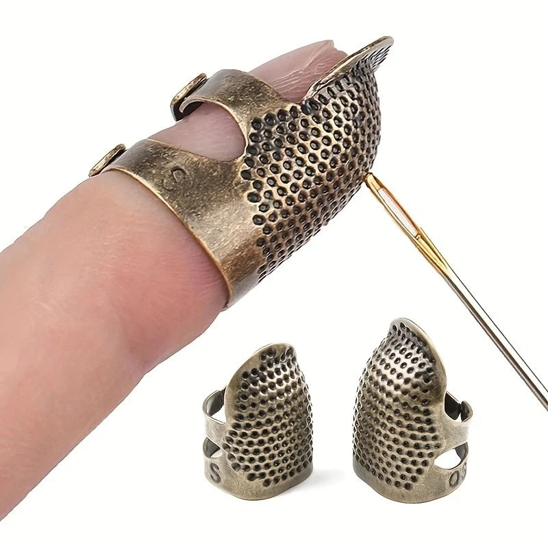 A hand holds an antique sewing thimble and needle protector set featuring textured brass or bronze metal pieces.