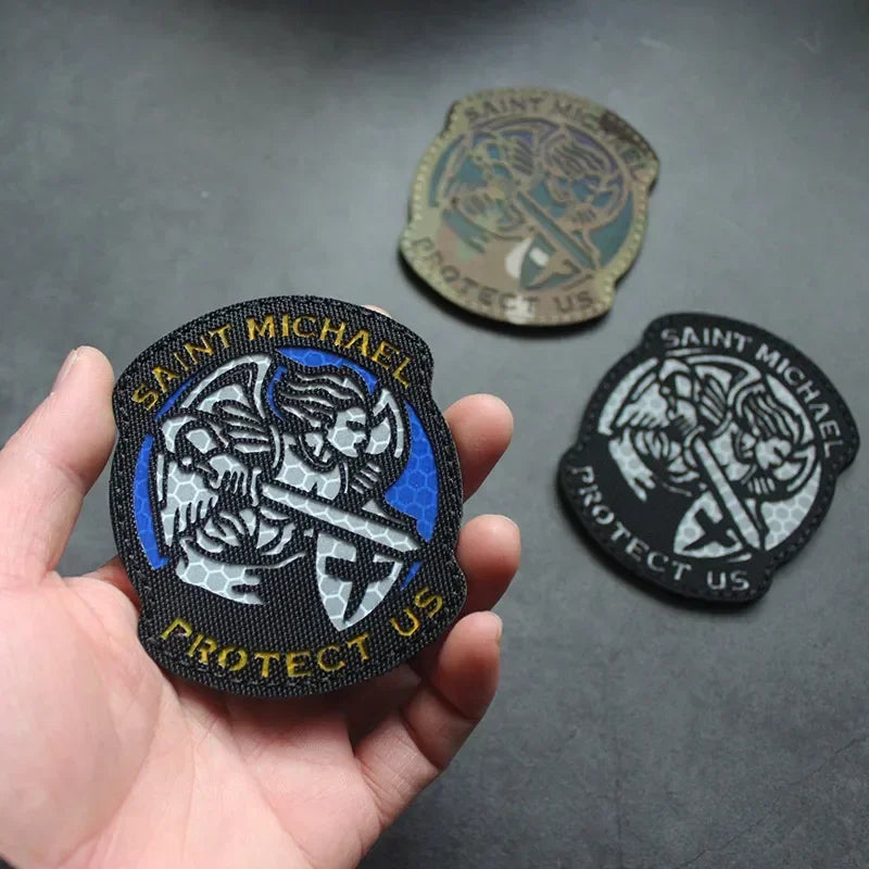 A hand holds an embroidered angel patch for tactical gear featuring a shield and text.