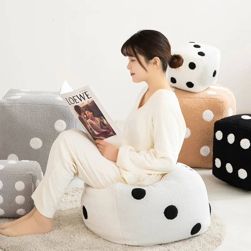 A woman is sitting on a white plush cube cushion surrounded by various polka-dotted and textured cushions.
