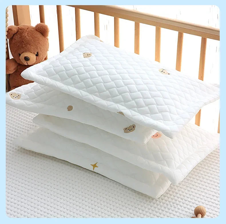 A stack of white quilted cooling pillows with small bear designs resting on a white surface.