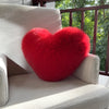 A bright red, heart-shaped plush throw pillow made of fox fur resting on a light-colored sofa.