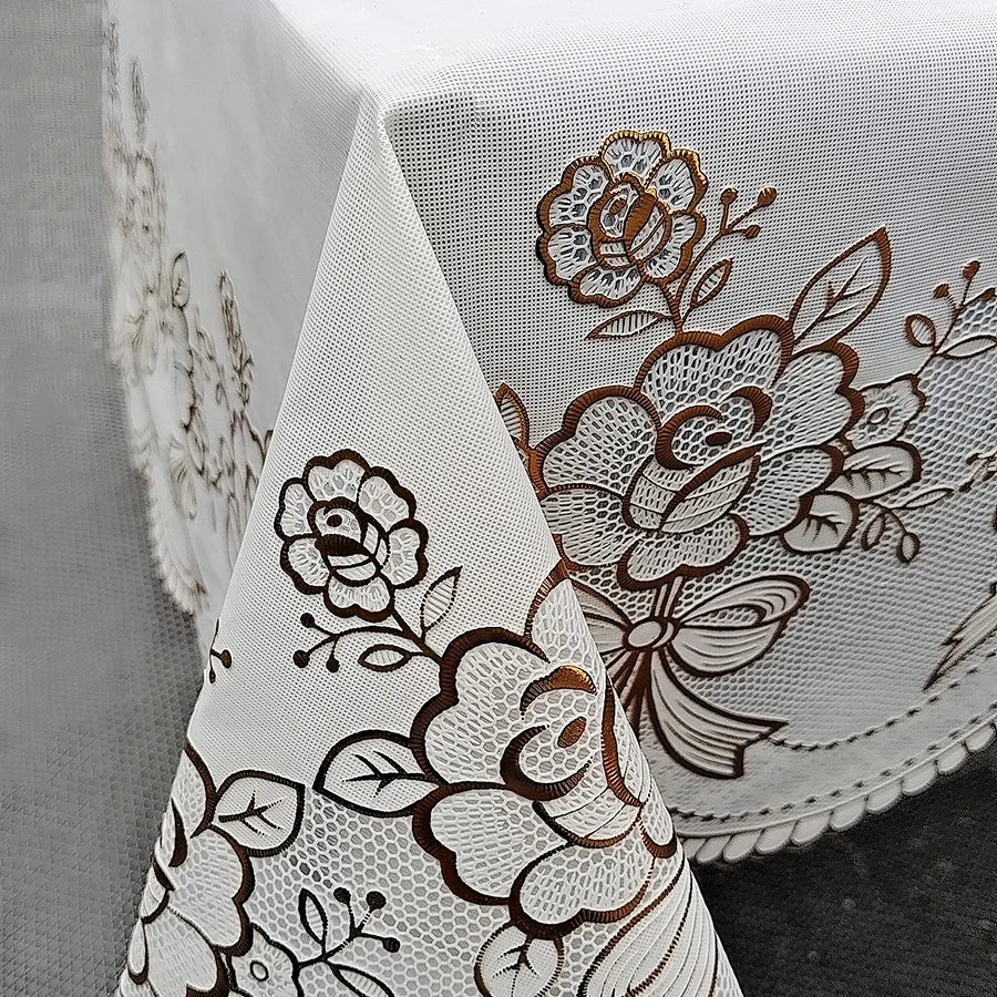 Close-up of a white lace dining table cloth featuring brown floral embroidery on a gray fabric background.