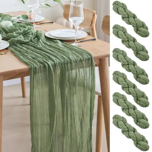 Green cheesecloth table runner draped on a wooden table with white plates and glassware.