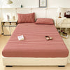 A neatly made bed with a red and white checkered fitted sheet, pillows, and bedside table in a bright room.