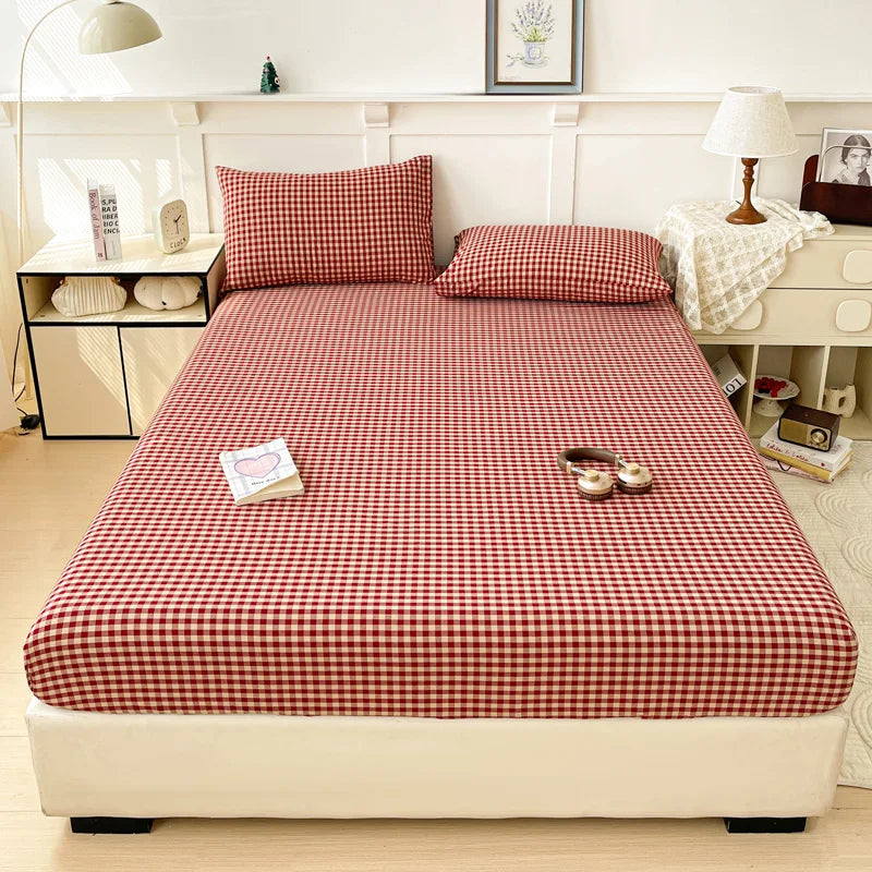 A neatly made bed with a red and white checkered fitted sheet, pillows, and bedside table in a bright room.