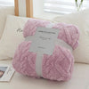 A fluffy pink plush throw blanket with a white strap and a silver tag is displayed on a white surface.