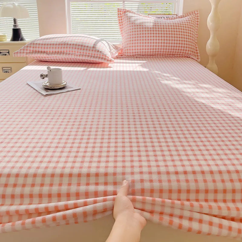 A pink and white gingham flannel fitted sheet is laid out on a bed with matching pillows.