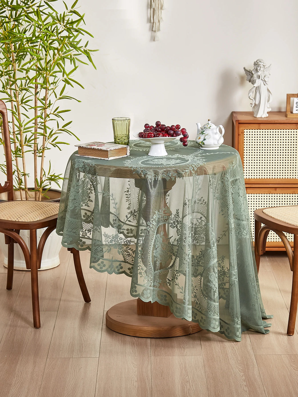 A round floral lace tablecloth in sage green with a tatting weave displayed on a wooden table.