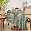 A round floral lace tablecloth in sage green with a tatting weave displayed on a wooden table.