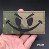 A close-up of a tactical multicam national flag patch with a menacing, angry face design being held in a hand.