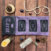 A purple fabric pouch for storing tarot cards, surrounded by pine cones, stones, and a tarot card.