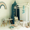 A white wooden canopy bed decorated with teal curtains and stuffed toys, set in a bright room.