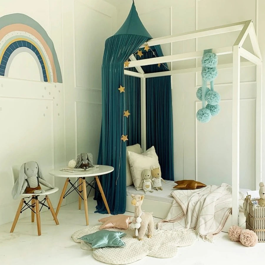 A white wooden canopy bed decorated with teal curtains and stuffed toys, set in a bright room.