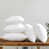 A stack of white cotton-filled decorative throw pillow inserts resting on a wooden surface.