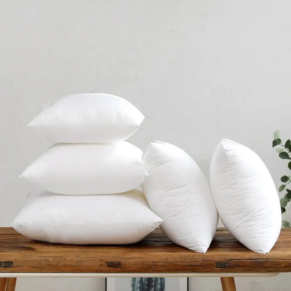 A stack of white cotton-filled decorative throw pillow inserts resting on a wooden surface.