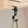 A black adjustable desk hook with dual clips is shown hanging from a light green strap.
