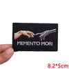 Black embroidered patch with the text MEMENTO MORI in light gray thread