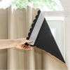 A hand is adjusting a black blackout curtain with a gray hook and loop closure on a light-colored fabric.