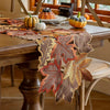 A rustic farmhouse maple leaf table runner made of brown and orange leaves is displayed on a wooden table.