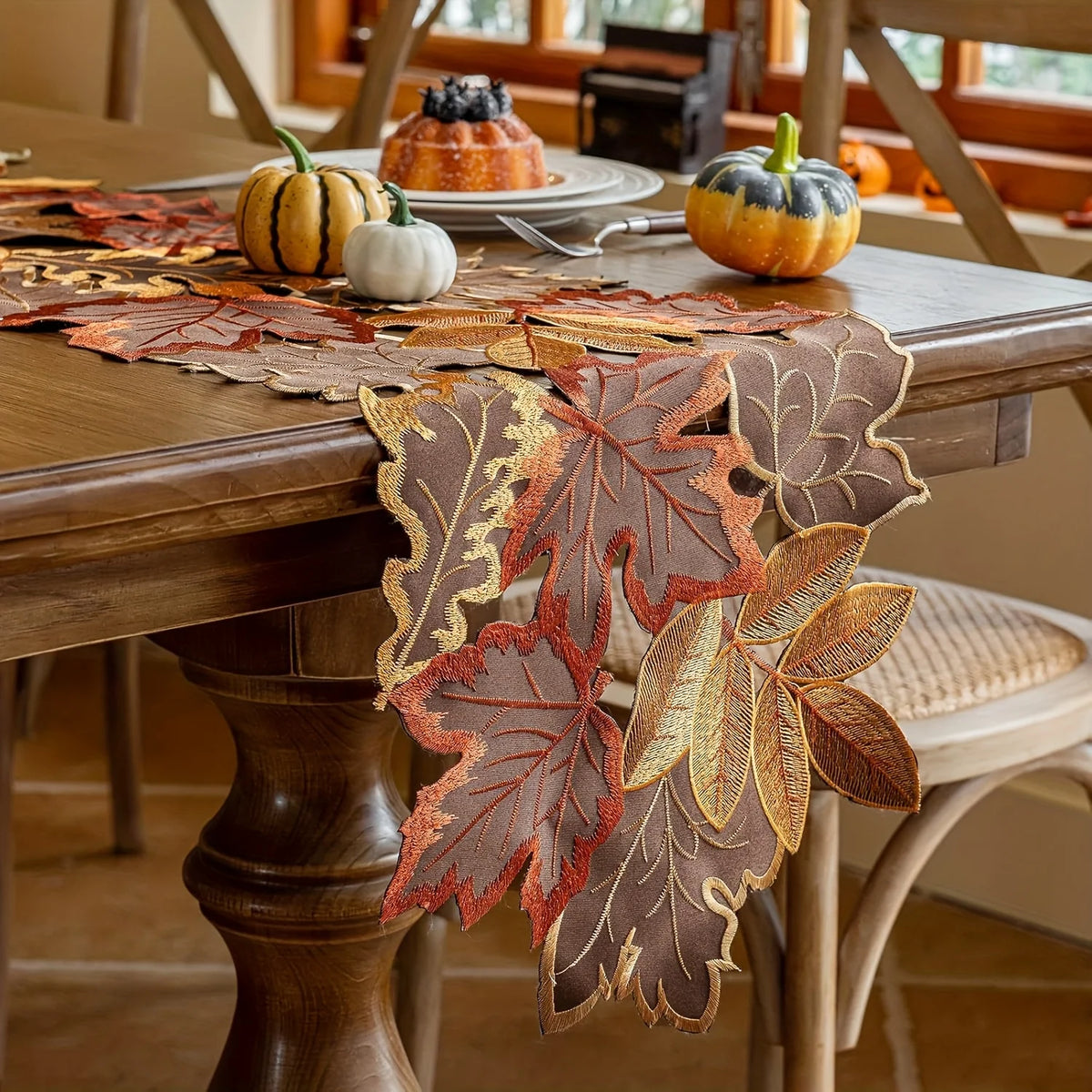 A rustic farmhouse maple leaf table runner made of brown and orange leaves is displayed on a wooden table.