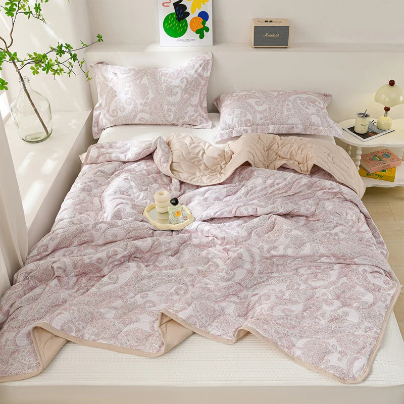 A pink lightweight cooling summer quilt set displayed on a white bed with pillows and decorative items.