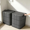 A gray foldable storage bag with a black lid is shown standing on a light floor next to a white wall.