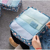 A blue patterned storage organizer set with six folded light blue and white clothes inside, being opened by a hand.