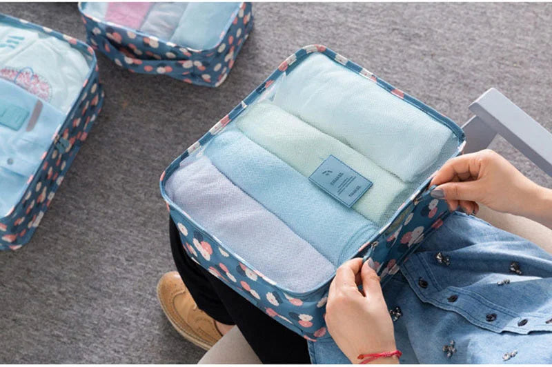 A blue patterned storage organizer set with six folded light blue and white clothes inside, being opened by a hand.