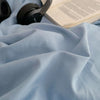 A close-up of a light blue linen fabric draped on a surface next to headphones and an open book.