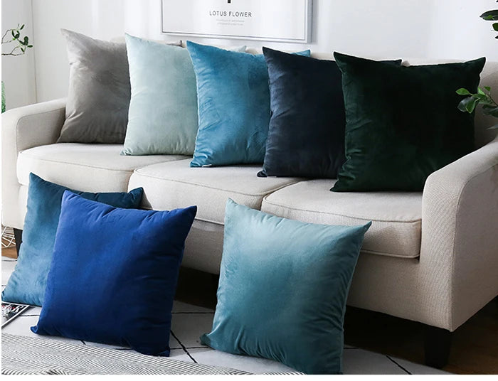 A collection of teal, blue, and dark green velvet cushion covers arranged on a light-colored sofa.