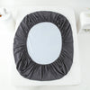 A round waterproof mattress and bed protector sheet in dark gray fabric placed on a white surface.