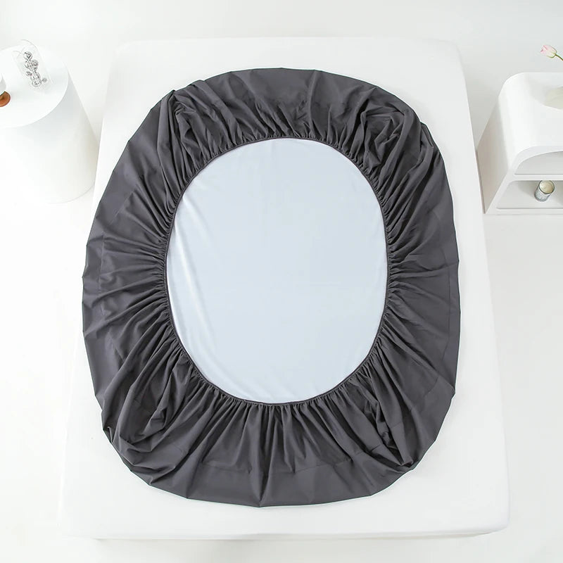 A round waterproof mattress and bed protector sheet in dark gray fabric placed on a white surface.