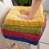 A stack of colorful tufted corduroy floor seat cushions in yellow, green, pink, and blue.