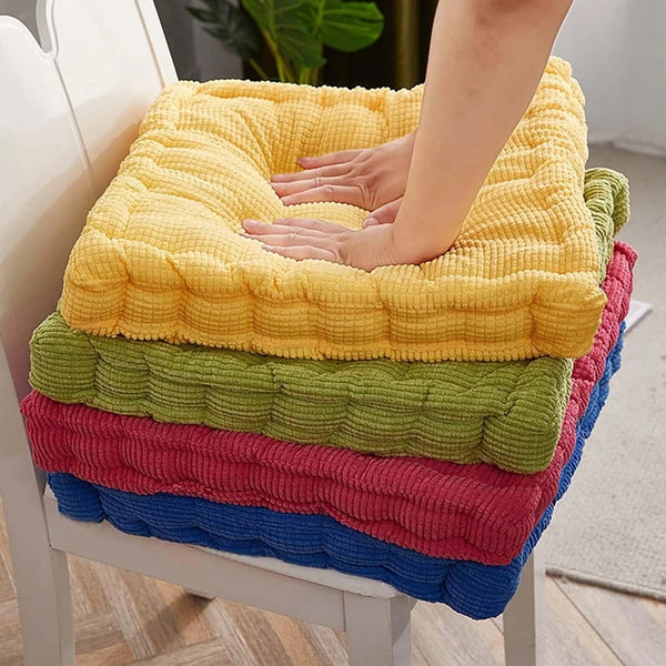 A stack of colorful tufted corduroy floor seat cushions in yellow, green, pink, and blue.
