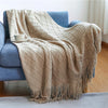 A beige knitted tassel throw blanket draped over a blue sofa.