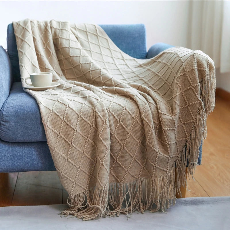A beige knitted tassel throw blanket draped over a blue sofa.