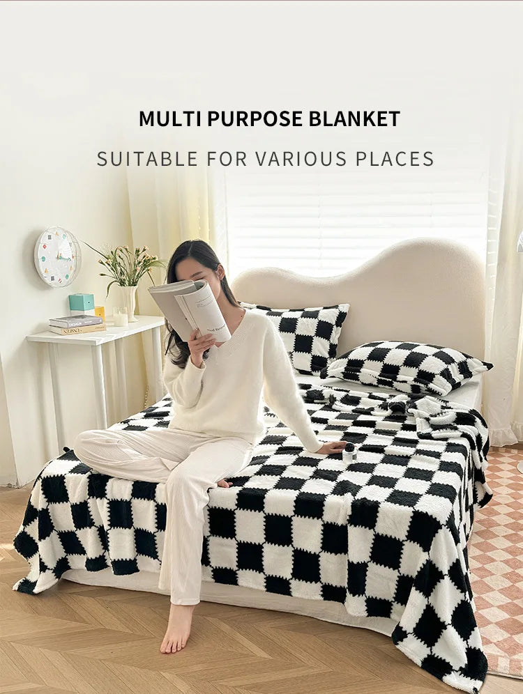A person is sitting on a bed covered with a black and white checkered blanket, wearing a white top and pants.
