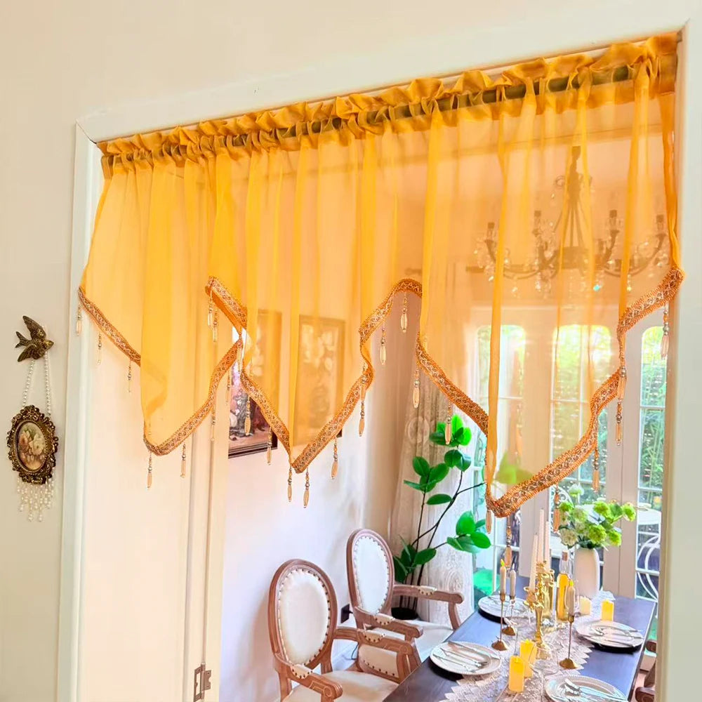 A sheer yellow curtain with gold lace trim and tassels hangs in a bright room.