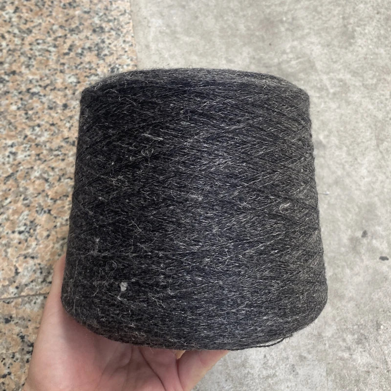 A dark gray hand-woven wool and linen blended yarn is tightly wound on a spool, held in a person's hand.