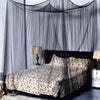 A queen size mosquito net canopy draped over a bed with floral patterned bedding and bedside lamp.