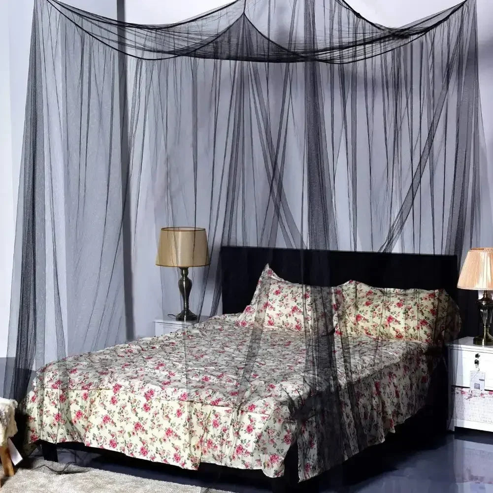 A queen size mosquito net canopy draped over a bed with floral patterned bedding and bedside lamp.