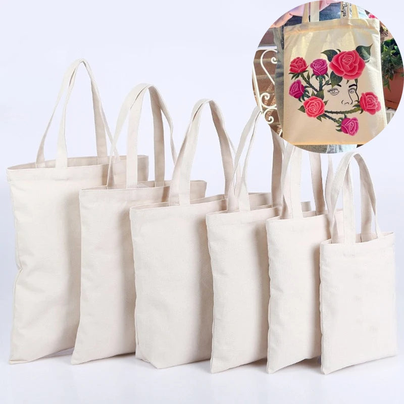 A set of natural canvas tote bags in cream and beige colors, with one bag featuring a floral design.